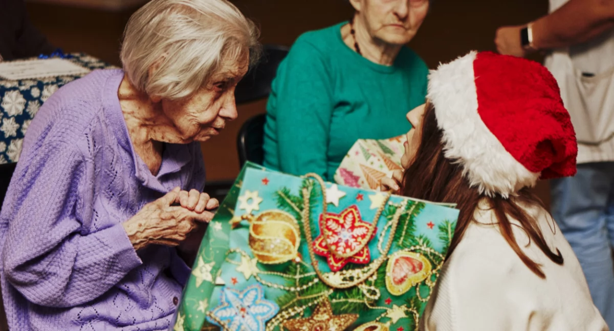Zdjęcie przedstawia darczyńcę wręczającego paczkę seniorce