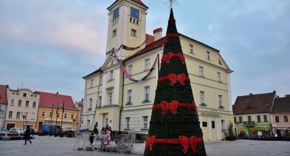Zdjęcie przedstawia Rynek w Kościanie z choinką i szalem